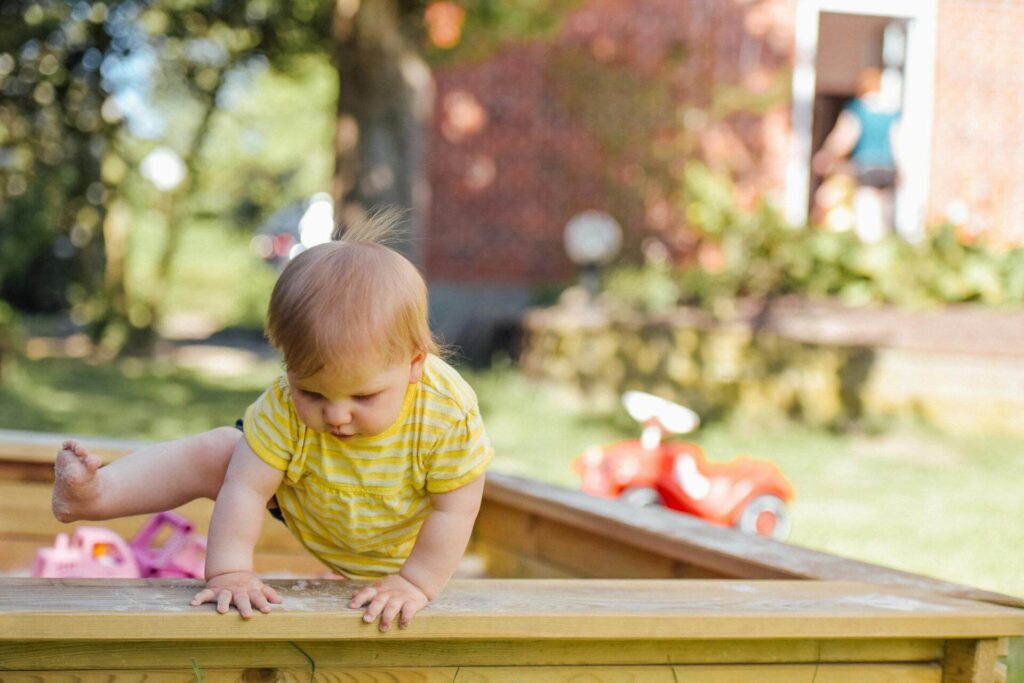 Baby climbing out of sandbox outdoors