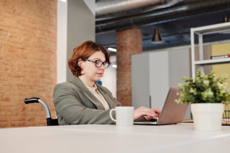 Professional woman in a wheelchair working on a laptop at a contemporary workspace.