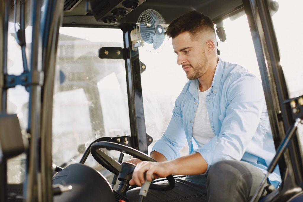 A young man is focused on driving a modern tractor with precision. The sunlight highlights the indoor setting.