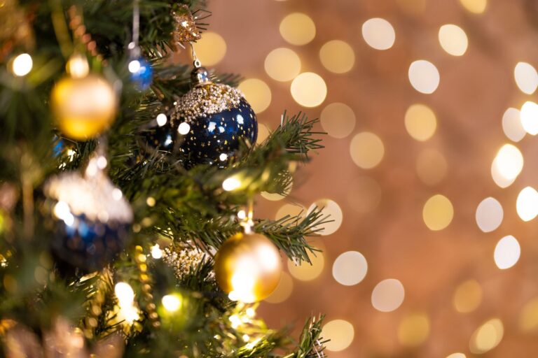 Close-up of a beautifully decorated Christmas tree with blue and gold baubles and bokeh lights.