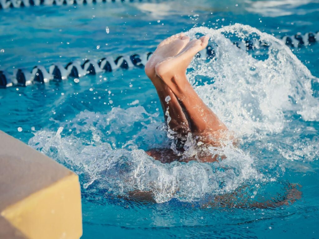 Close-up of swimmer's legs emerging through water splash in a pool, highlighting motion and activity.